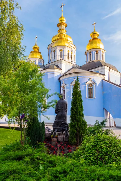 Невелика скульптура, що стоїть біля красивої церкви з куполами, сяючим золотом на сонці і хрестами на них . — стокове фото