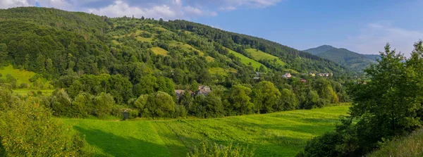 Kleine Bauernhäuser im Schatten grüner hoher Bäume an den Hängen sanft abfallender Berge — Stockfoto