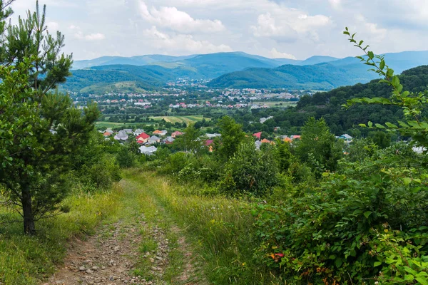 斜坡上的道路上镶嵌着石头, 上面有一幅美丽的风景, 上面躺着一个风景如画的山谷里的村庄的屋顶和房子。. — 图库照片