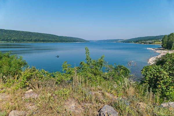 Güzel bir sonsuz mavi göle arka planı yeşil dağların ortasında bir teknede bir balıkçı