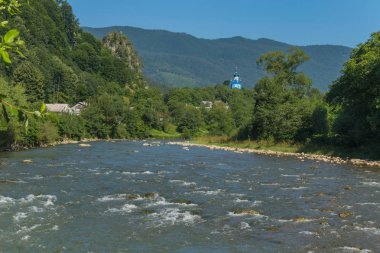 Hızlı dağ nehir arka planı mavi üstündeki kilise kilise, küçük evler ve rocky Dağları