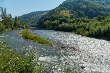 bir dağ eteğinde düşük yeşil plajlar arasında çalışan bir serinletici nehir