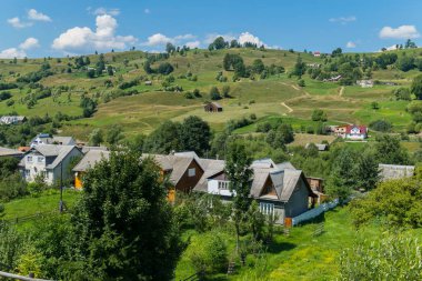 yeşil çim ve ağaçların yakınlarında dağınık renkli evler bir vadi üzerinde bir köy