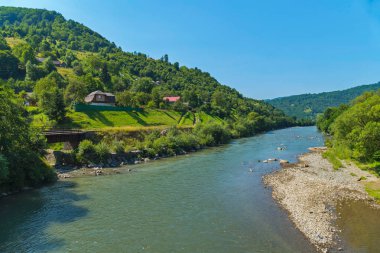 geniş dağ nehir kolları ve yeşil tepelerin arka plan üzerinde köyü yakınlarında kayalık kıyıları ile