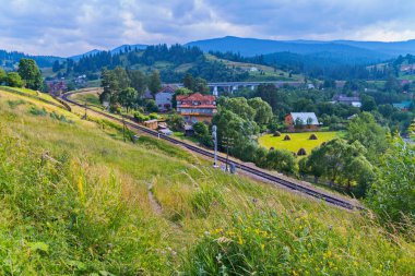 Çim ve pürüzsüz yapar demiryolu aşağıdaki için önde gelen çiçekler ile büyümüş bir yamaç üzerinde bir yol köy evleriyle dön.