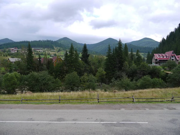 Aldeia pela estrada entre as montanhas cercadas por árvores verdes sob o céu nublado. lugar de descanso, turismo, piquenique — Fotografia de Stock