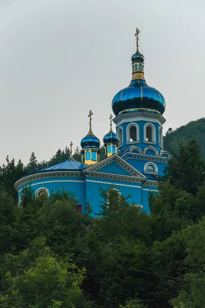 Синя православна церква серед зелених високих дерев під блакитним безхмарним небом — стокове фото