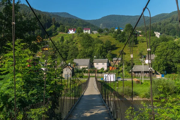 Hängebrücke über einen schnellen Fluss, die zu einem kleinen ländlichen Dorf in den Bergen führt — Stockfoto