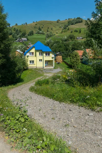 Uma estrada de montanha que leva a uma casa de campo amarela com um telhado azul contra uma alta inclinação verde — Fotografia de Stock