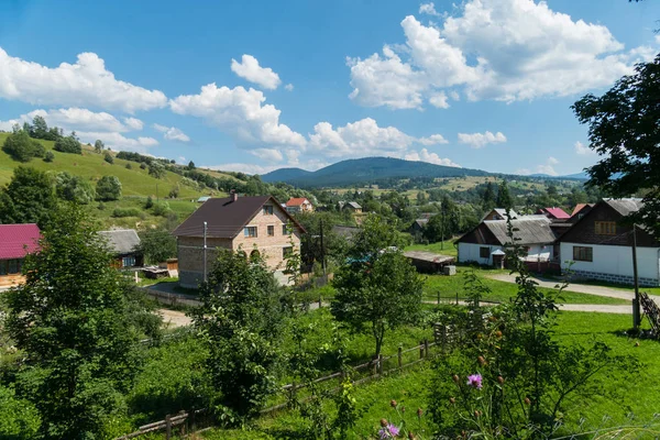 Moderne und alte private Wohnhäuser mit Gartengrundstücken und Obstbaumgärten in einem Dorf in einem Bergtal unter blauem wolkenverhangenem Himmel. Ort der Ruhe und des Tourismus — Stockfoto