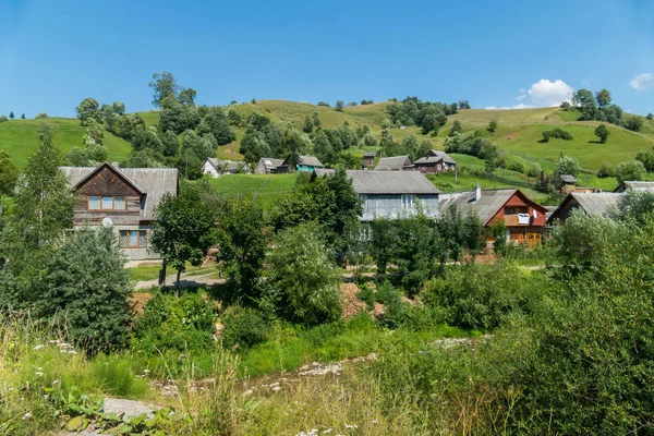 2 階建てのコテージや緑の山と青い空の背景の小さな家と村 — ストック写真