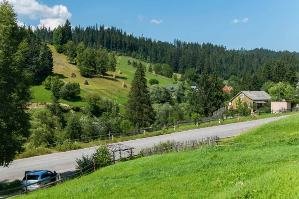 A country road on the slope of a green mountain and small houses — Stock Photo, Image
