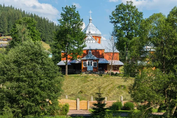 Μια μικρή όμορφη ξύλινη εκκλησία με μια στέγη και ασημί θόλοι με φόντο ένα καταπράσινο δάσος και ένα γαλάζιο ουρανό — Φωτογραφία Αρχείου