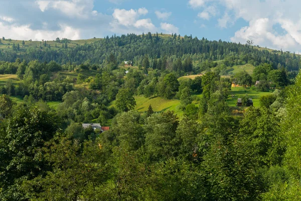 Panorama z zielonymi wzgórzami i gdzieś dachach domów rozglądać się wśród zieleni — Zdjęcie stockowe