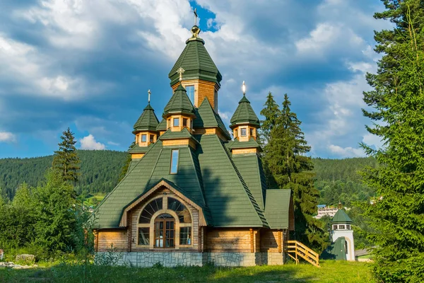 Uma enorme igreja de madeira com um telhado verde contra um majestoso fundo de montanha e um céu azul nublado — Fotografia de Stock