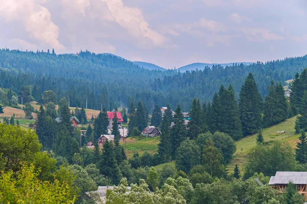 Grüne Wälder und Berge blauen Himmels mit Wolken und ein kleines Dorf im Tal — Stockfoto