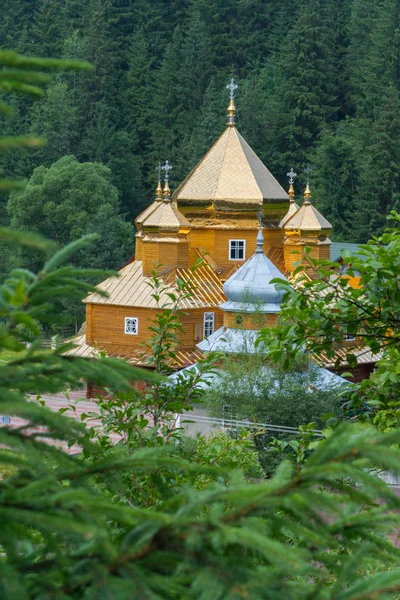 A beautiful wooden church amidst green nature and thick trees with domes that cast gold in the sun. — Stock Photo, Image