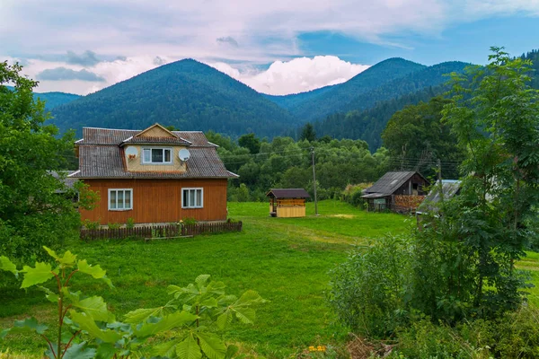 Egy kis vidéki ház egy udvar és egy régi jól a háttérben a zöld-hegység és fehér felhők — Stock Fotó