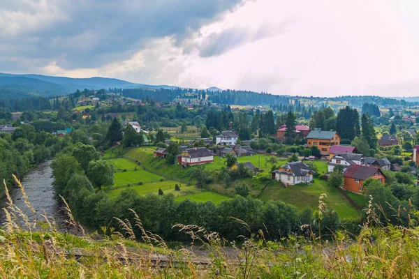 çayır üstünde küçük bir köy ile Zarflama yeşil bankalar arasında akan nehir dağ