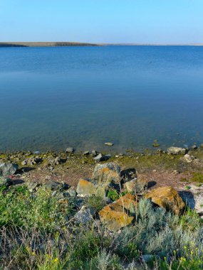 Keskin taşlar bir şeffaf mavi göl kıyısında yeşil yosun kaplı