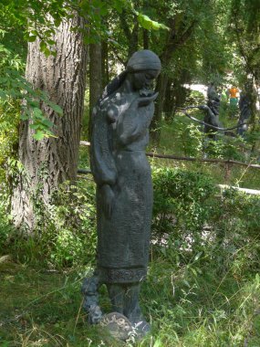 Kollarında bir ağacın altında bir parkta bir zambak olan kırılgan bir kadın heykeli. Sergi turistler için