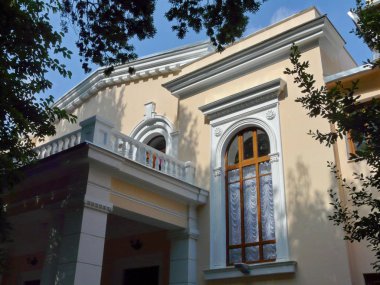 Uzun boylu pencere ve balkon beyaz raylar ve yanında büyüyen ağaçlar ile duvara sıva ile güzel bir bina cephe.