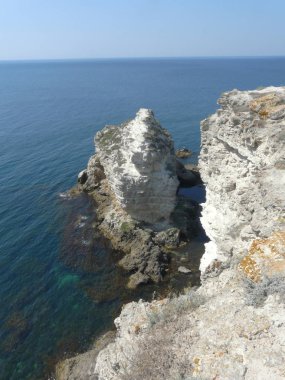 Rocky, dik bir banka ile mavi deniz. Kayalar sahile uzak kırdı