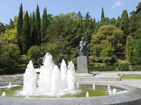 bir üstün oturan adam uzun boylu yeşil ağaçlar ve bulutsuz mavi gökyüzü arka planı kesilmiş çalılar çevrili yuvarlak bir çeşme önünde bir anıt