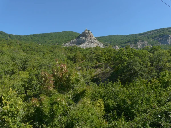 Скалистая вершина с памятником посреди заросших деревьев холмов — стоковое фото