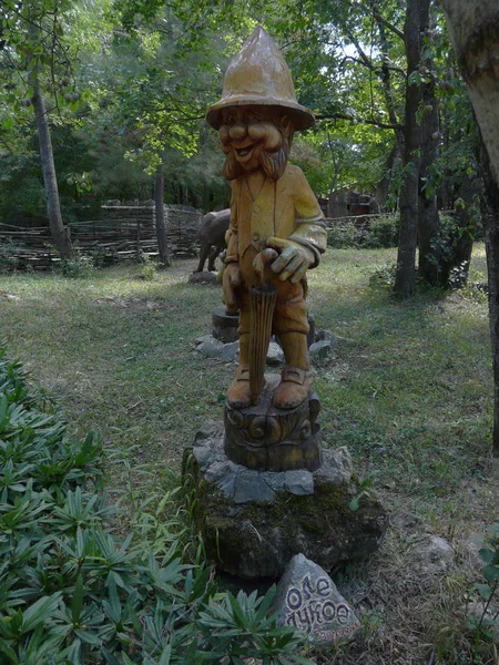 En trä staty av en gnome med ett paraply i handen står på en klippa i parken — Stockfoto