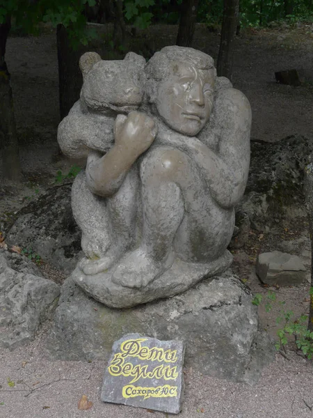 Escultura en el parque sentado en el suelo de un hombre con un pequeño oso detrás de él, situado en una piedra baja . — Foto de Stock
