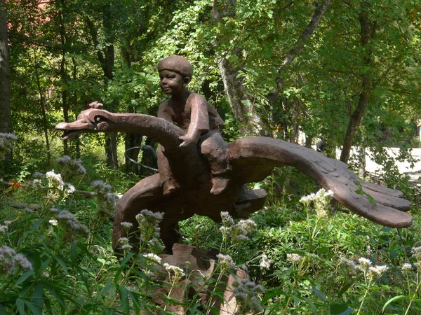 Skulptur av en pojke som sitter grensle en flygande gås mot en bakgrund av grönt gräs — Stockfoto