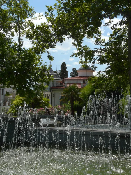 Transparant verfrissende fonteinen met transparante water in het park met mensen op de bankjes rusten. — Stockfoto