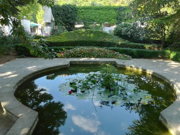 Ein künstlicher Teich mit Lilien, umgeben von einem Granitstein, und um ein grünes Blumenbeet — Stockfoto