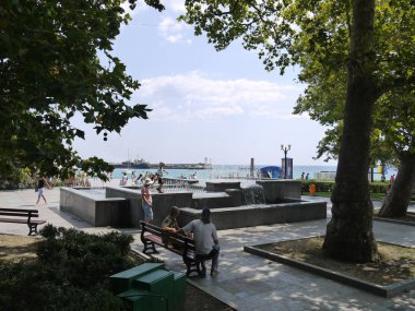 Parktaki insanlar sahildeki bir çeşmenin yanında banklar üzerinde dinleniyor