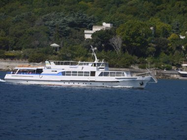 Kar-beyaz zevk tekne turist mavi denizin kıyısında yeşil yamaçları zemin karşı düşük dalgaların arasında yüzen.