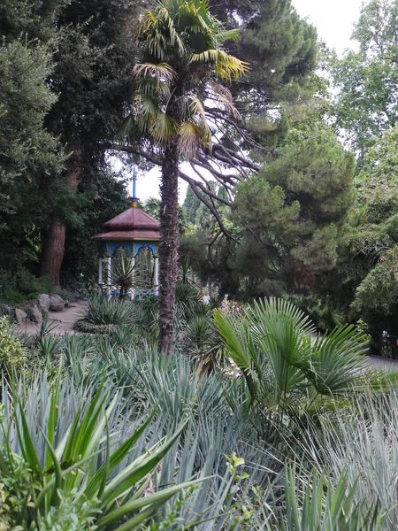 Prieel voor rust in het park met een hoge puntige spits staan onder de struiken van struiken en planten. — Stockfoto