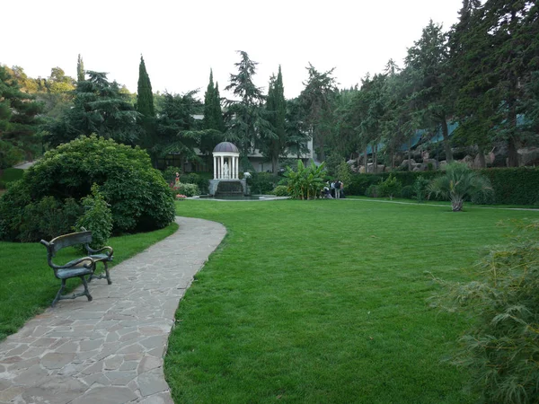 Una vecchia panca con schienale in legno per il riposo. In piedi vicino alla passerella in un pittoresco parco con una bella natura . — Foto Stock