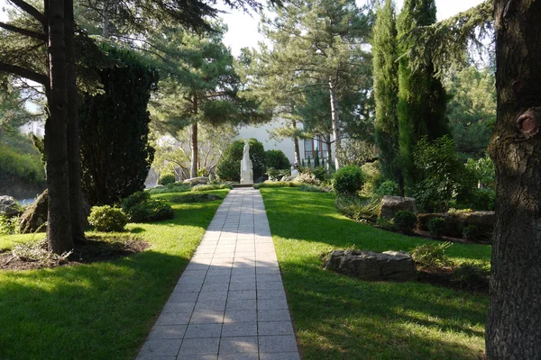 A tiled walkway with green trees on either side leading to a stone sculpture — Stock Photo, Image