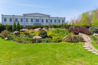 Alışılmadık bir dikdörtgen binanın dekoratif çalılar ve taş ile yeşil bir flowerbed arka planı