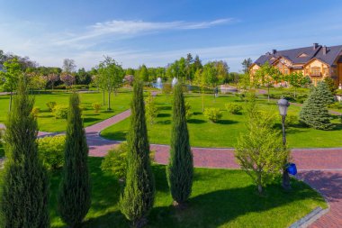 taş yolları, yeşil çim, piramidal Mazı (bitki), yaprak döken ağaçlar, çeşmeler mavi bulutsuz gökyüzü altında bir gölet ile ahşap bir konak önünde büyük bir çim. dinlenme ve Turizm