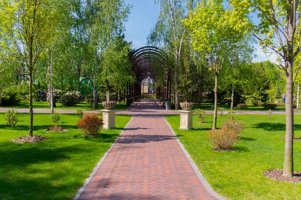 Camino en un hermoso parque verde a un callejón de madera arqueada con linternas con bisagras — Foto de Stock