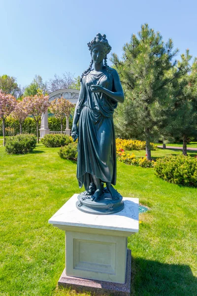 Metallskulptur einer Frau im antiken Stil auf einem weißen Ständer auf einem grünen Rasen — Stockfoto