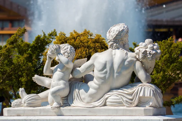 Skulptur av gips i form av en liggande mannen och pojken bredvid en bakgrund av buskar och stänk av en fontän — Stockfoto