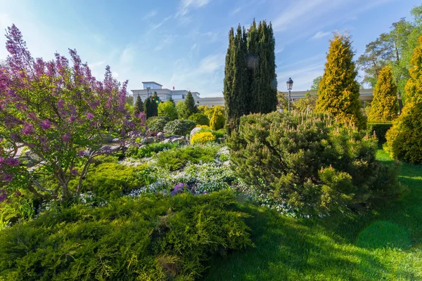 Suuri kukkapenkki, jossa on valtava valikoima pensaita, kukkia ja puita vihreällä nurmikolla — kuvapankkivalokuva