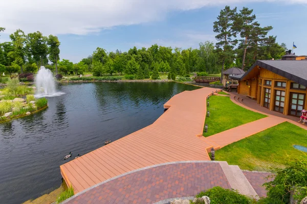 Una vista encantadora de la plataforma de madera de la orilla del estanque con los patos flotando a su lado y la fuente en el centro — Foto de Stock