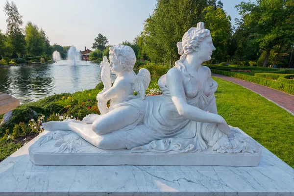 Weiße Statue einer liegenden Frau mit einem Engel am Ufer des Sees im Park. novi petrivtsi, ukrainisch — Stockfoto