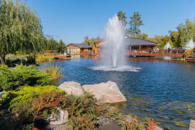 mavi gökyüzü altında bir çeşme ile küçük bir gölet yakınındaki mutlu turist