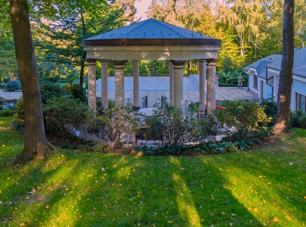 Um grande eixo para descanso com colunas que suportam o telhado com bancos e uma mesa dentro. Localizado em um parque com grama verde e bela natureza . — Fotografia de Stock