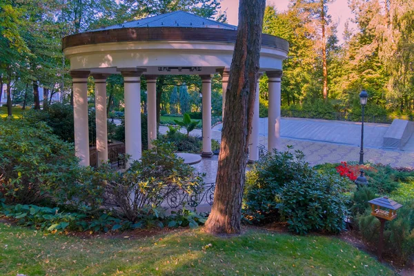 Gazebo decorativo com colunas brancas e cerca forjada contra o fundo de plantas verdes — Fotografia de Stock